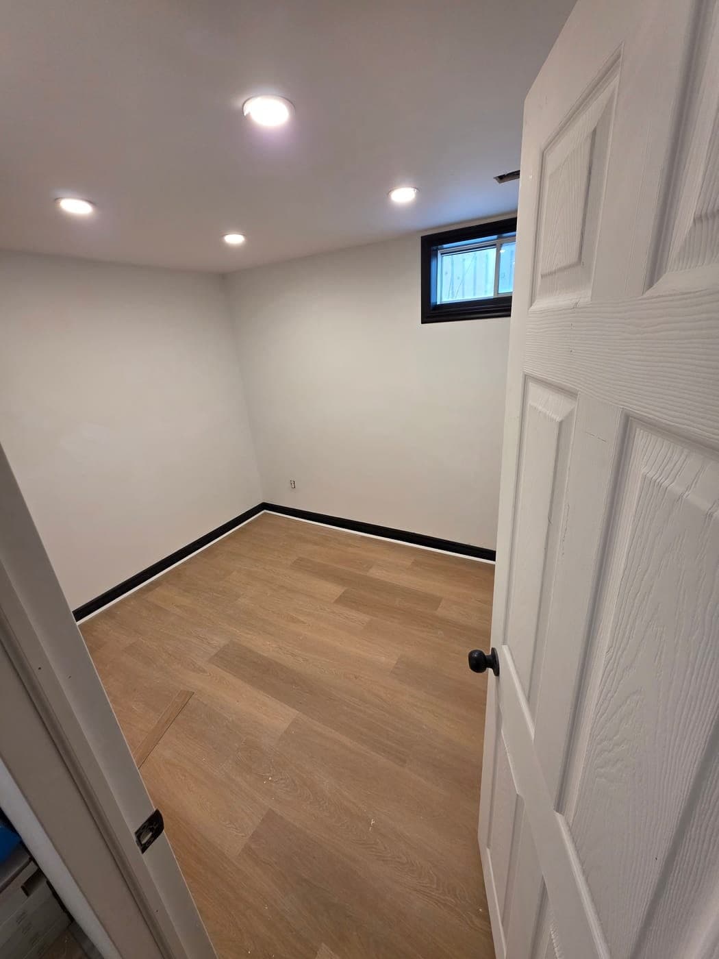 Finished basement bedroom with pot lights, wood-look flooring and black baseboards
