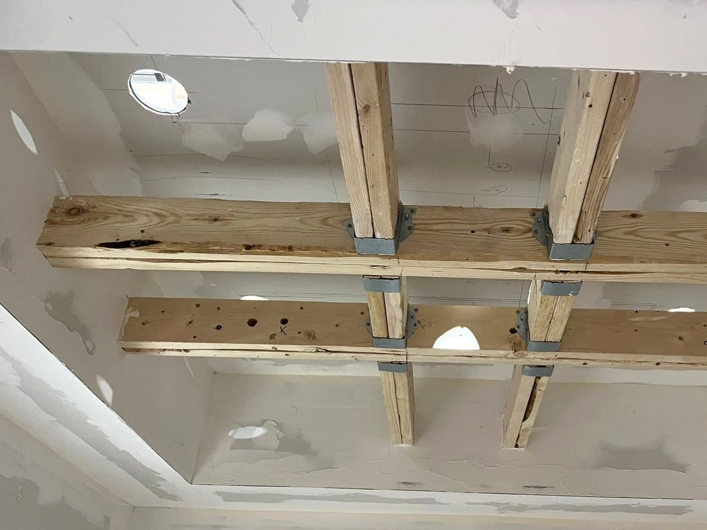 Coffered ceiling during construction: exposed wood beams joined with metal brackets in an unfinished drywall ceiling