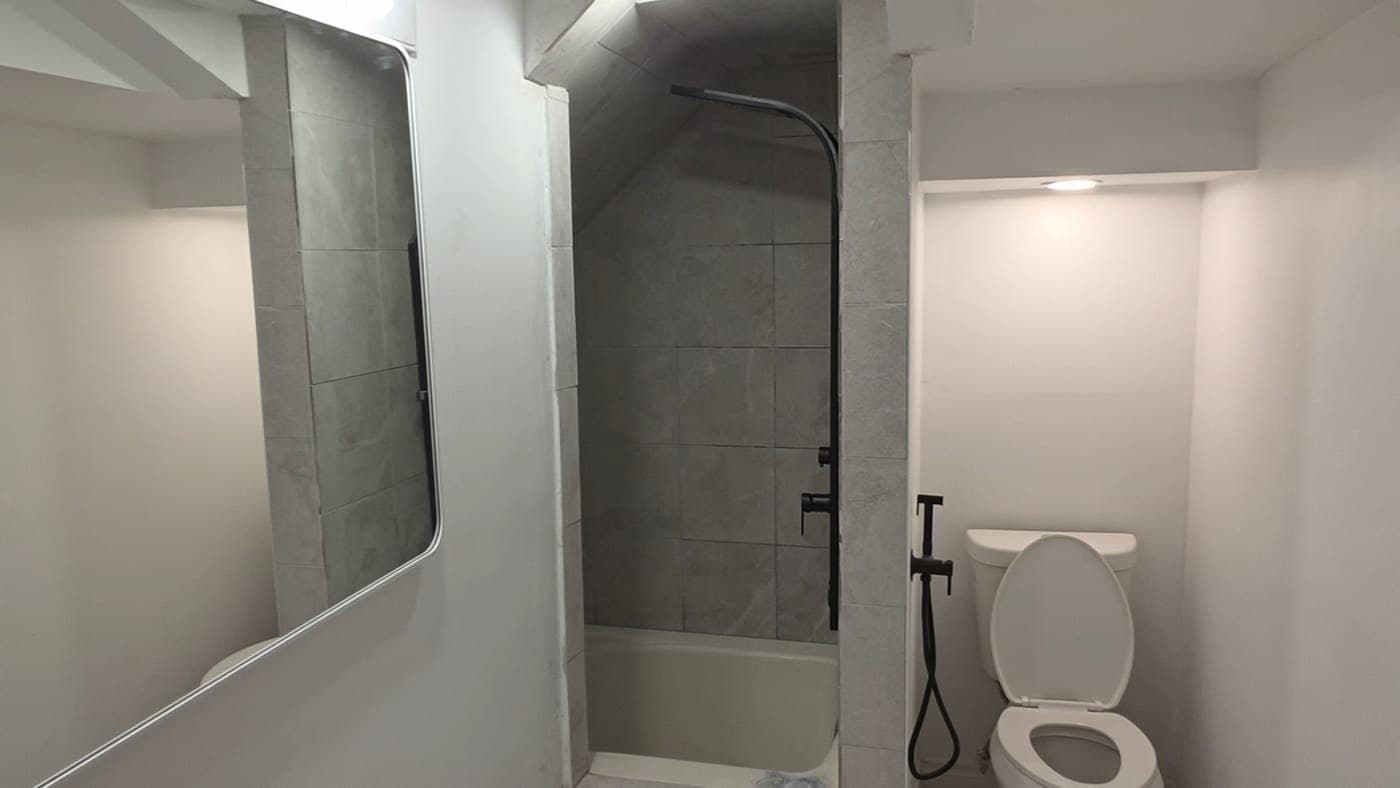 Basement bathroom with a tiled tub surround, black fixtures and a large mirror