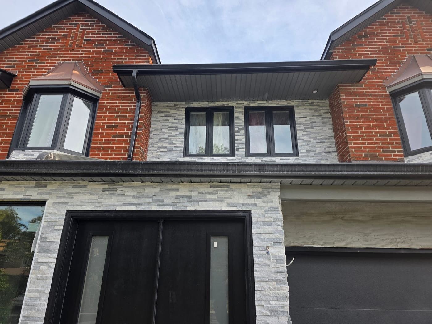 Close view of the rebuilt entry: stacked-stone cladding around black double doors with glass sidelights